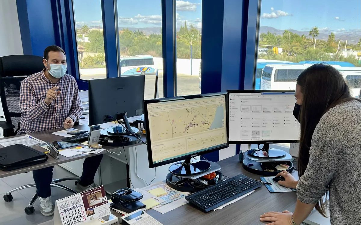 Dos personas trabajando con mapas de rutas y planificación de transporte en dos pantallas