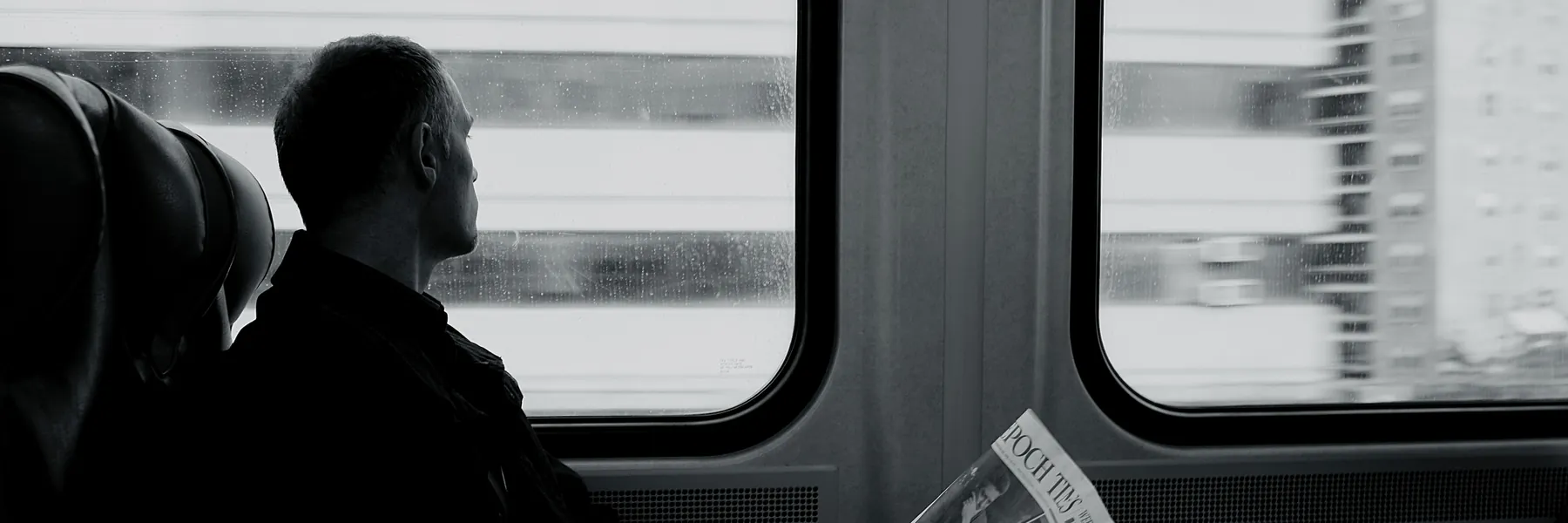 Una persona sentada junto a la ventanilla de un tren de cercanías, leyendo el periódico